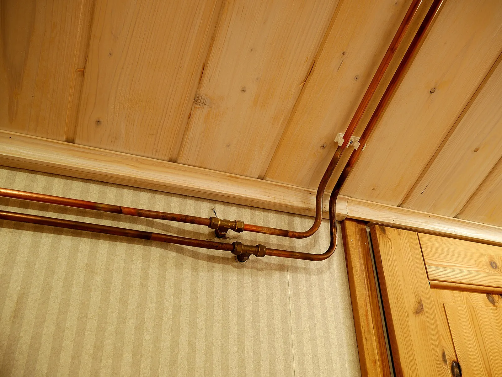 Copper water pipes running along a wood-panelled ceiling