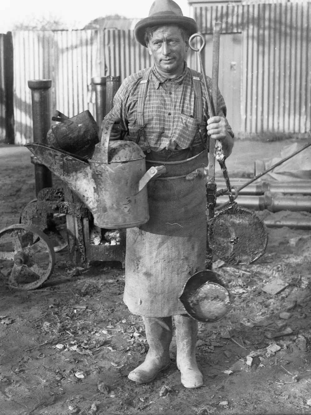 Black-and-white photograph of a plumber in an apron holding his tools, 1938